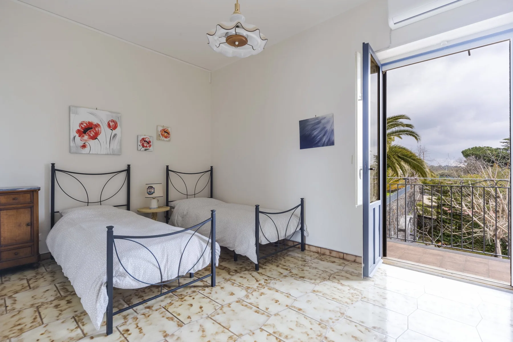 Un dormitorio luminoso con dos camas y puertas abiertas que dan a un balcón.