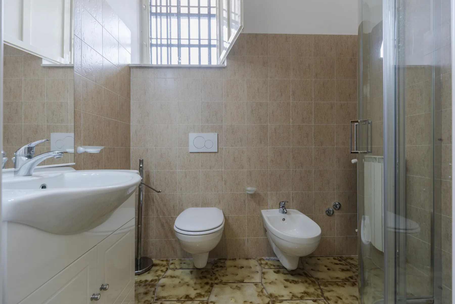 Un baño alicatado con lavabo, inodoro, bidé y ducha de cristal.