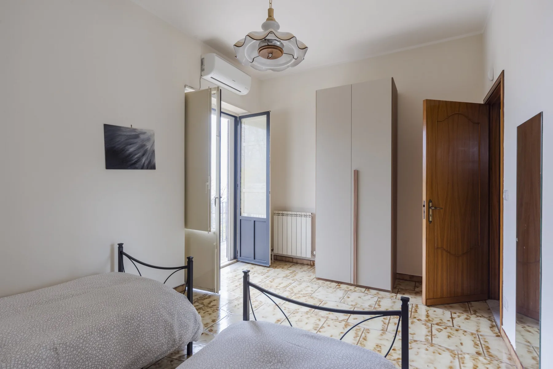 Un dormitorio con dos camas, un armario y una puerta abierta al balcón.