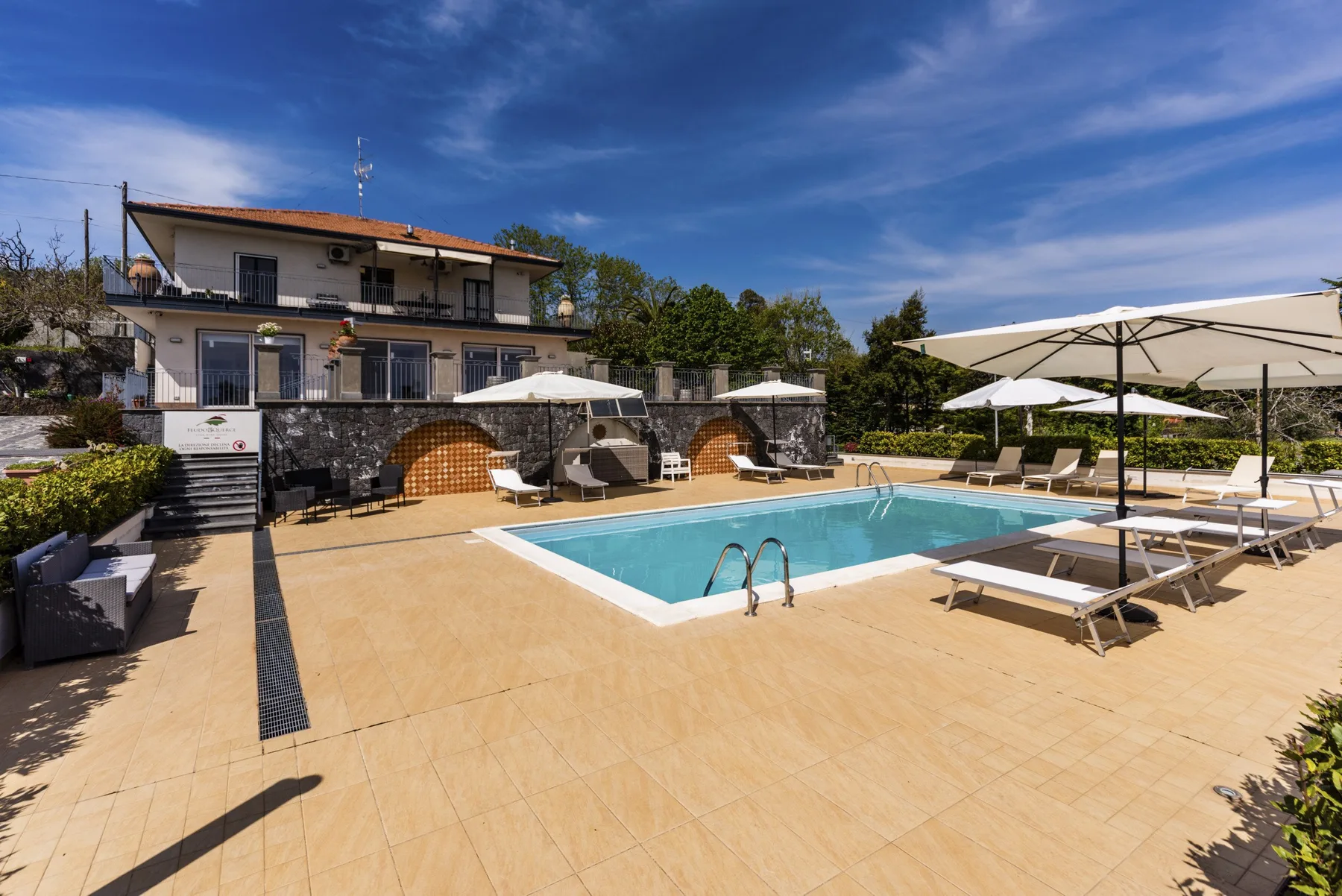 Una piscina al aire libre está rodeada por una terraza pavimentada y asientos.