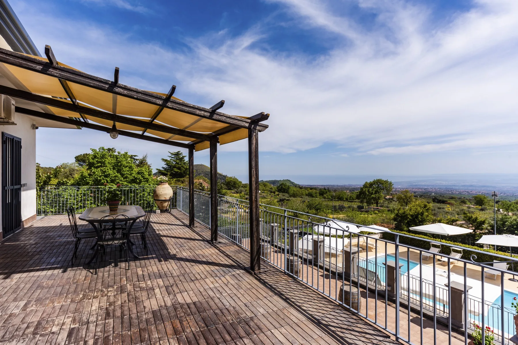 Una terraza de madera con pérgola da a una piscina y colinas verdes.
