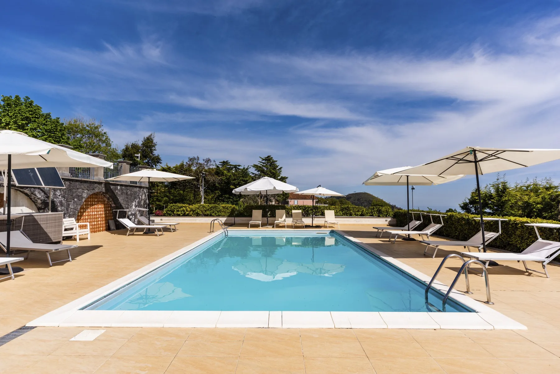 Una piscina al aire libre está junto a una terraza pavimentada con asientos y sombrillas.