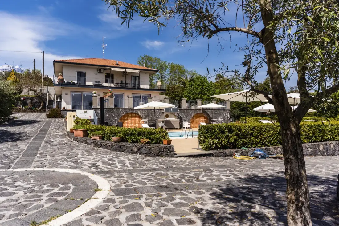 Una casa de dos plantas da a un patio pavimentado con piscina y zona de estar ajardinada.