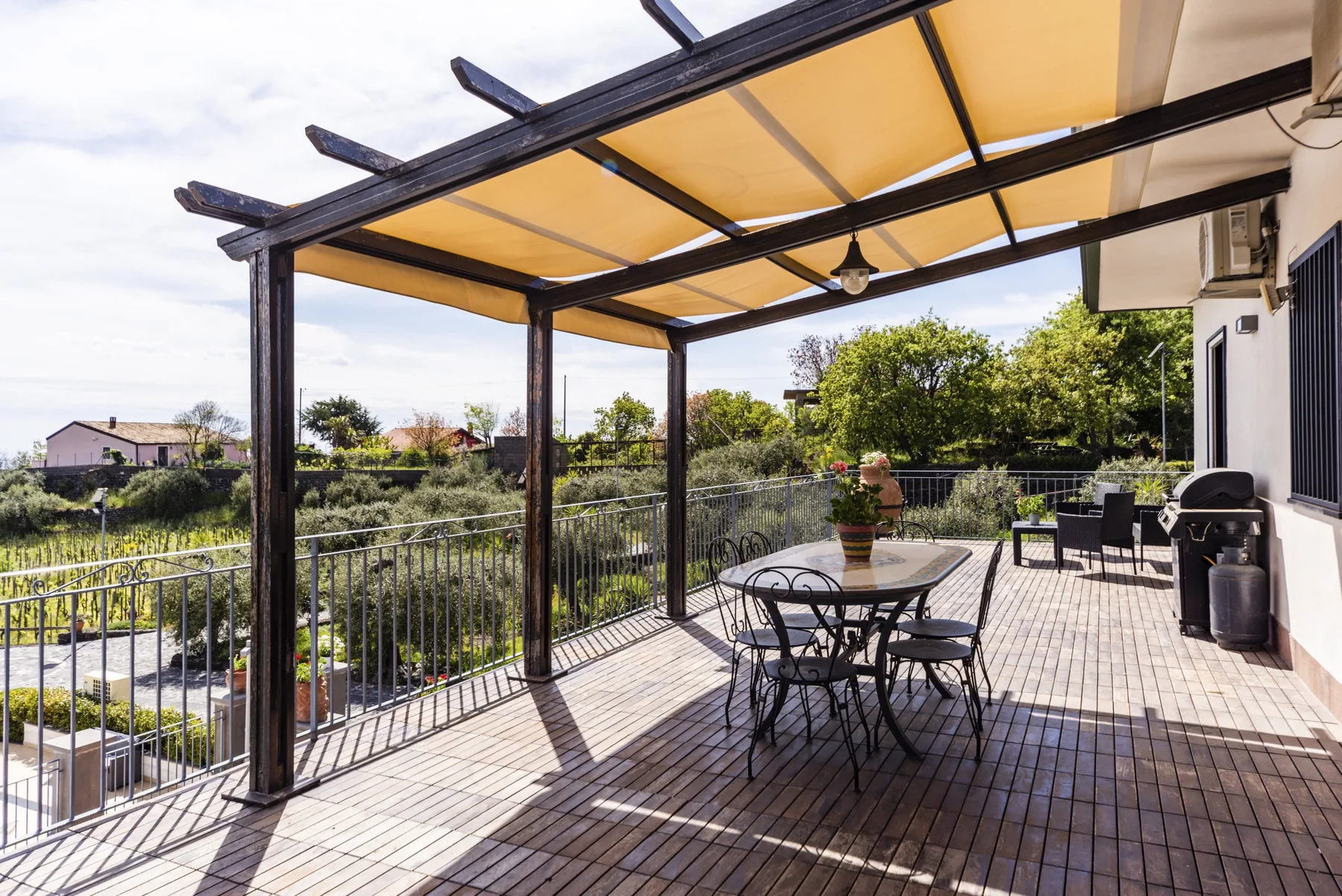 Una terraza exterior cubierta con mesa y asientos da a un jardín.