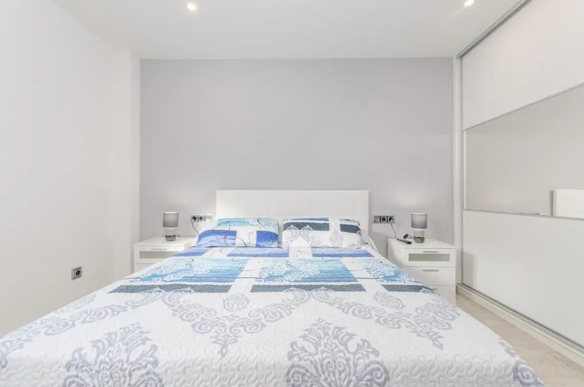 A bright bedroom with a bed, bedside tables, and a mirrored wardrobe.