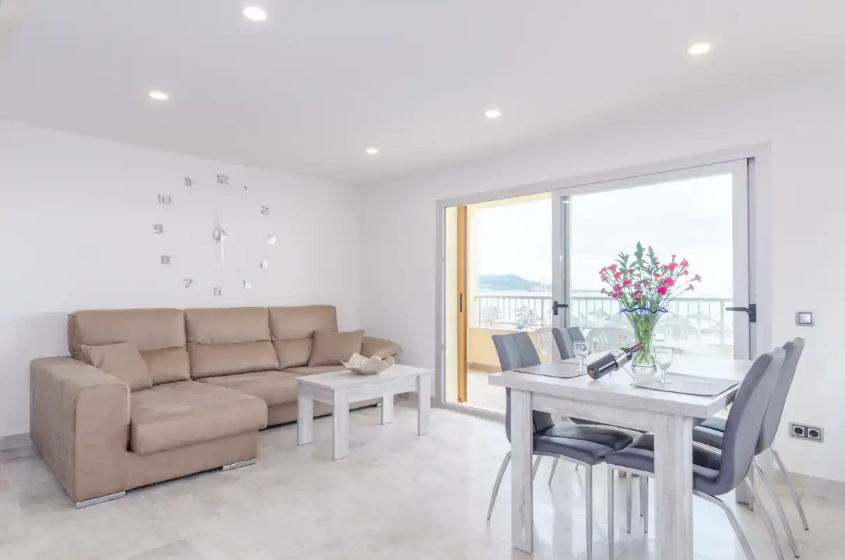 Bright living and dining area with a sofa, table, and balcony doors.
