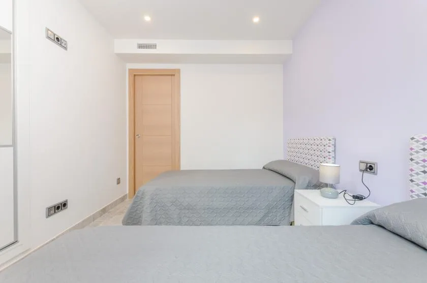 A bright bedroom with two beds and a bedside table.