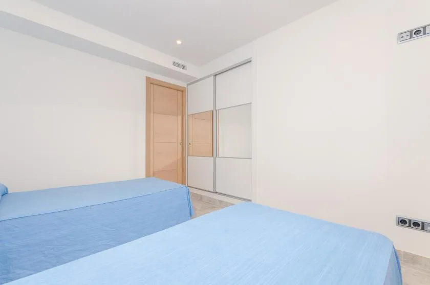 A bright bedroom with two blue beds and a mirrored wardrobe.