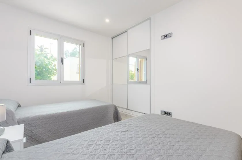 A bright bedroom with two beds and a window overlooking greenery.