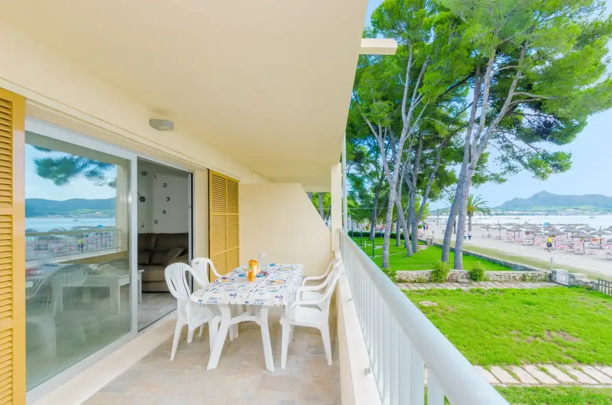A covered balcony with outdoor seating overlooks a green area and the coast.