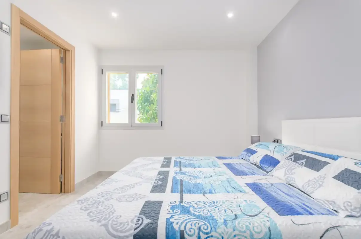 A bright bedroom with a bed covered in blue and white patterned bedding.