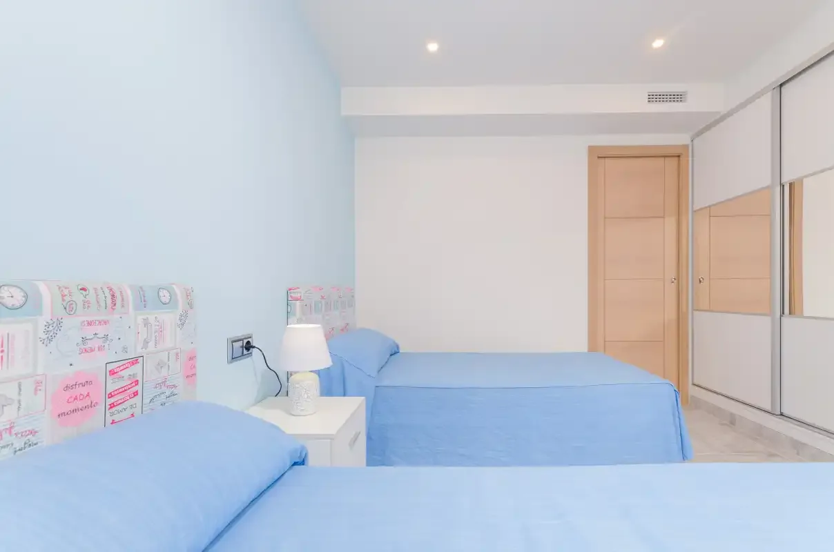 A bedroom with blue bedding, bedside tables, and mirrored wardrobes.