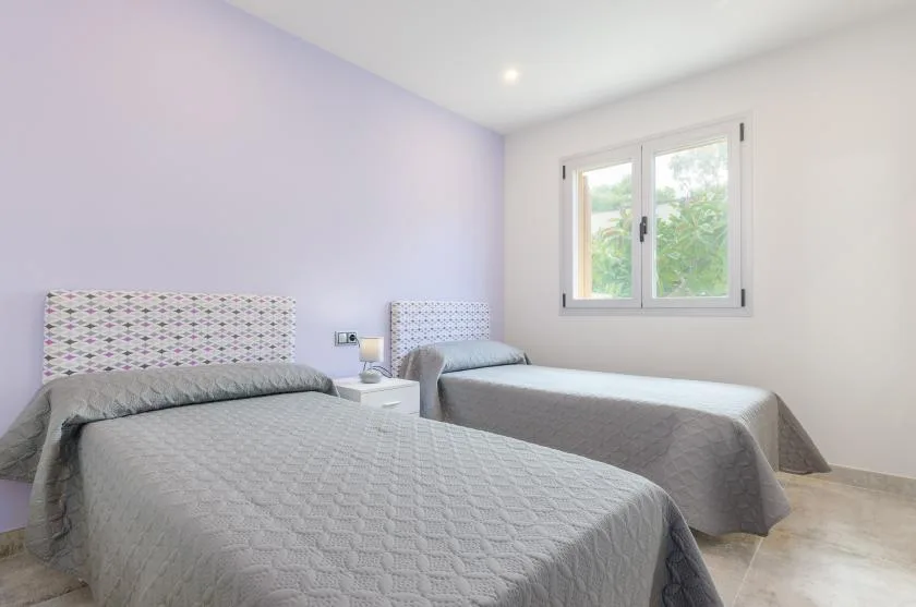 A bright bedroom with two beds and a window overlooking greenery.