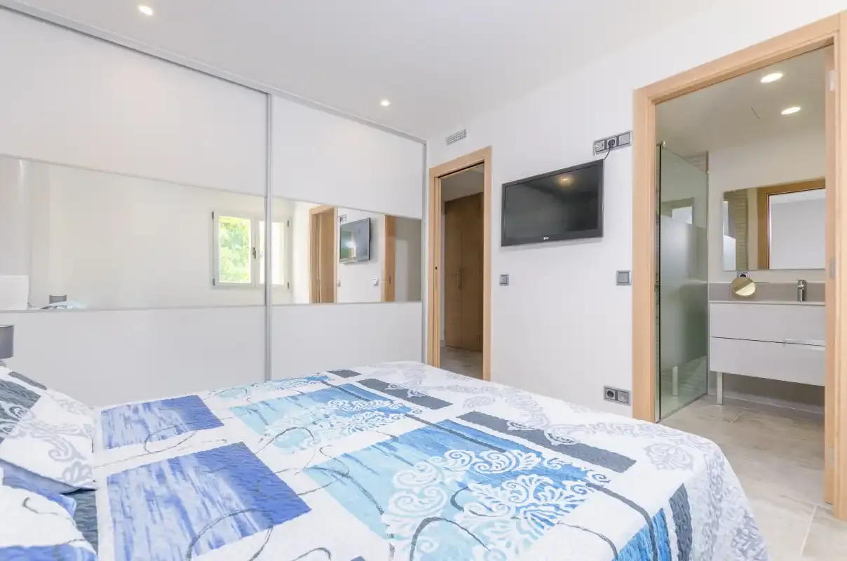 A bedroom with a bed, mirrored wardrobe doors, and a wall-mounted television.