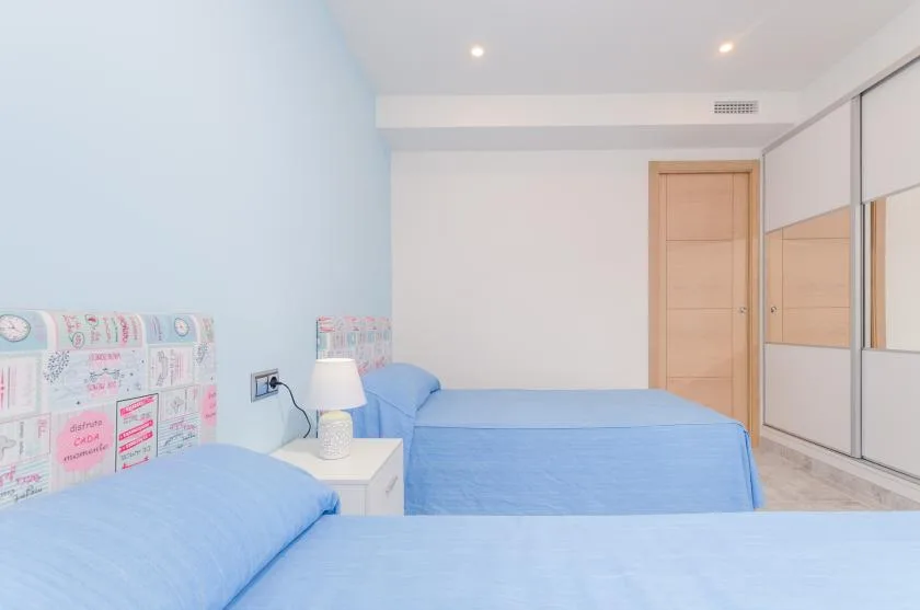 Bedroom with blue bedding, a bedside table, and mirrored wardrobe doors.