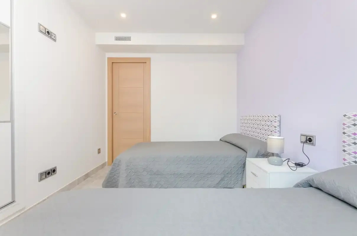 A bright bedroom with two beds and a bedside table.