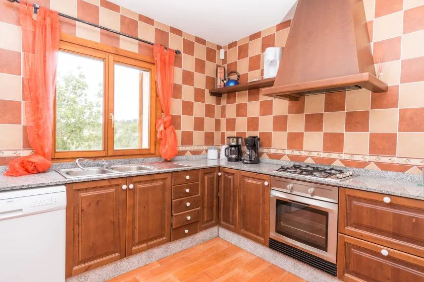 A kitchen with wooden cabinets, a countertop, and a window with orange curtains.