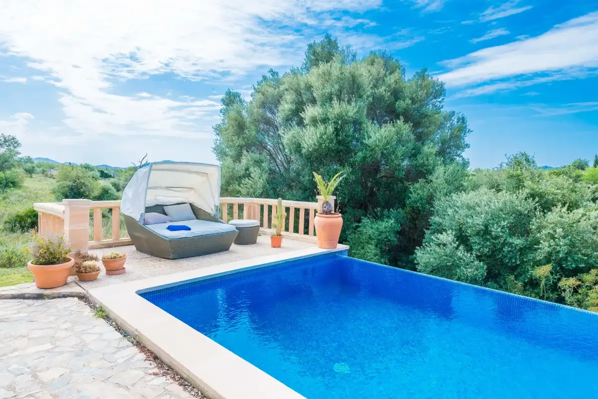 An outdoor swimming pool sits beside a terrace with potted plants and surrounding greenery.