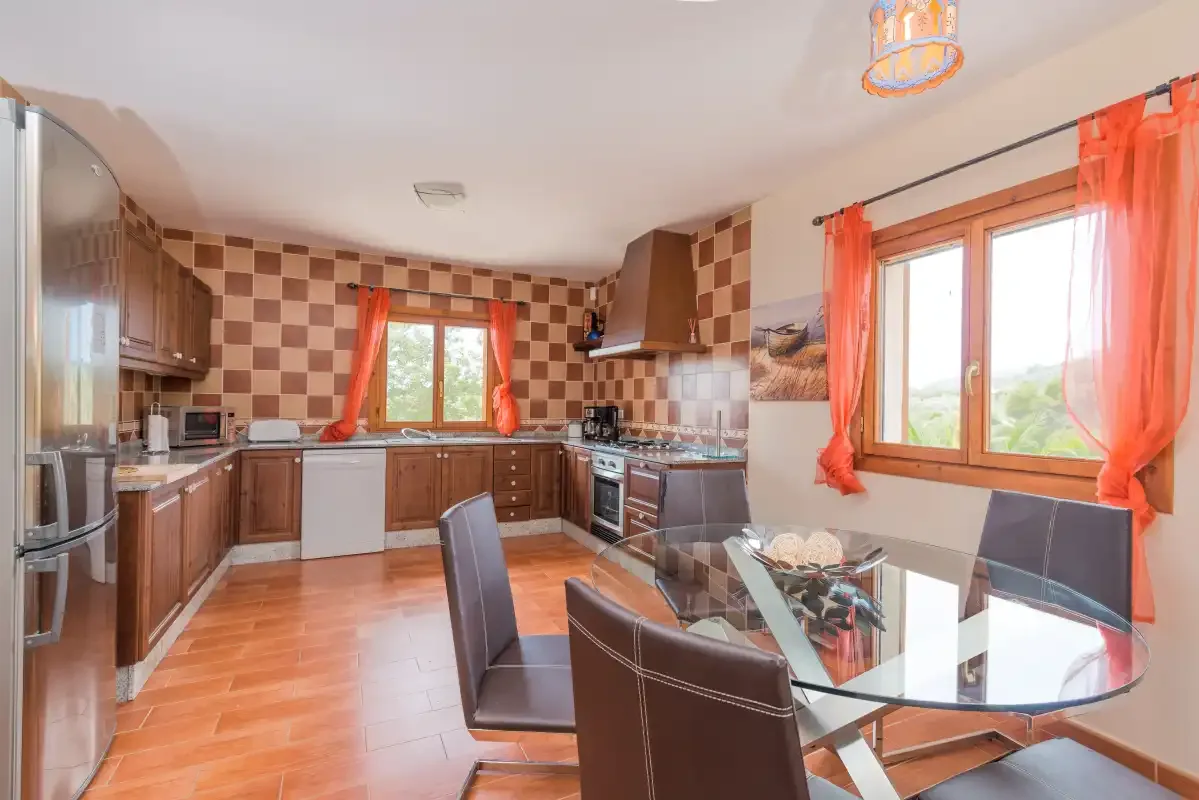 A kitchen and dining area with dark cabinetry, tiled walls, and a glass dining table.