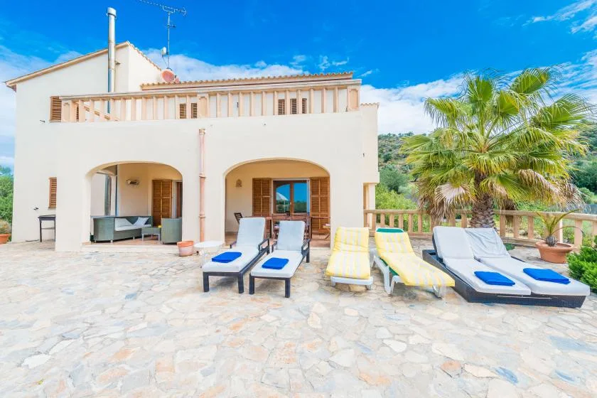 A sunny patio with lounge seating faces a light-colored house.