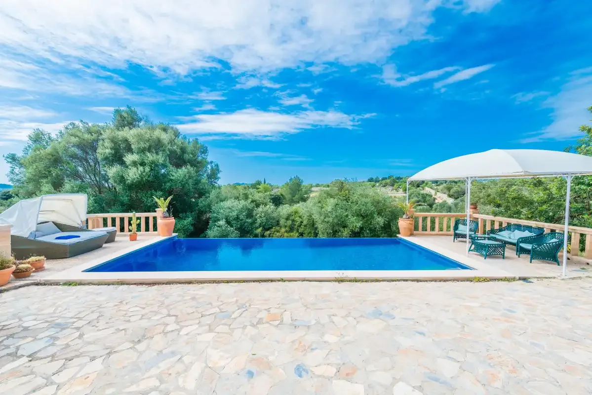 An outdoor swimming pool sits beside a paved terrace and shaded seating.