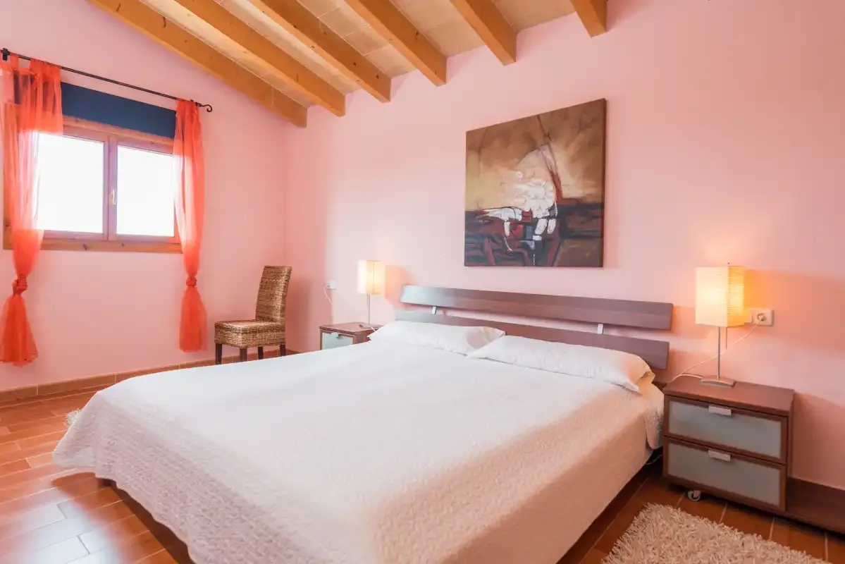 A bedroom with a large bed, bedside tables, and a window with orange curtains.