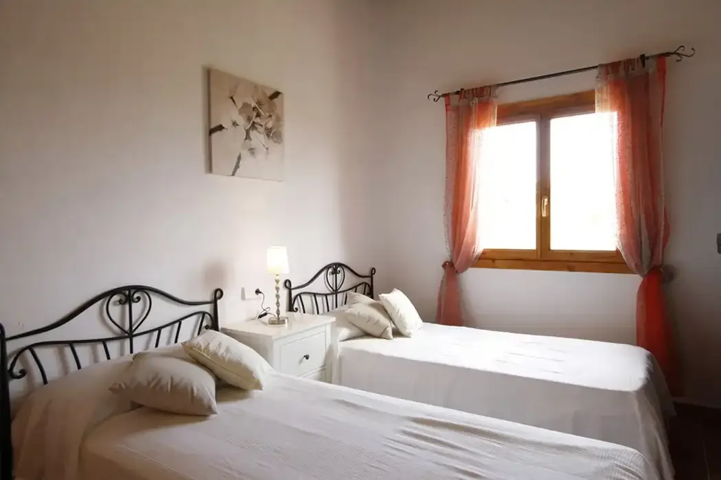 A bedroom with two beds, bedside tables, and a window with orange curtains.
