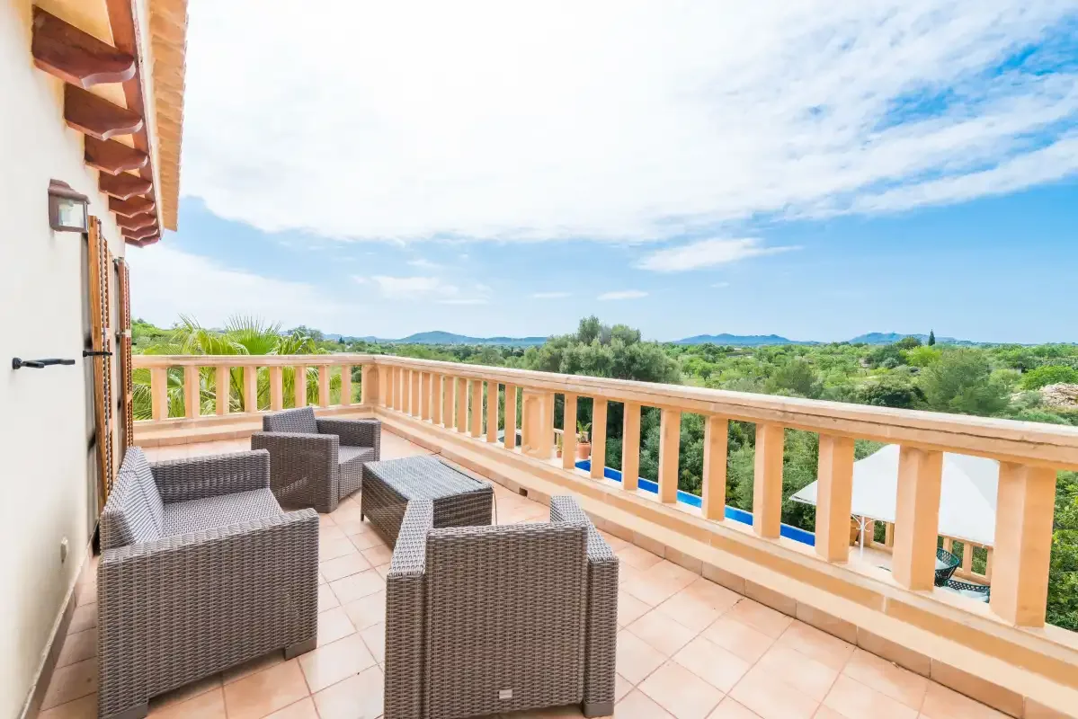 A tiled outdoor terrace has wicker seating and a wooden railing overlooking green countryside.