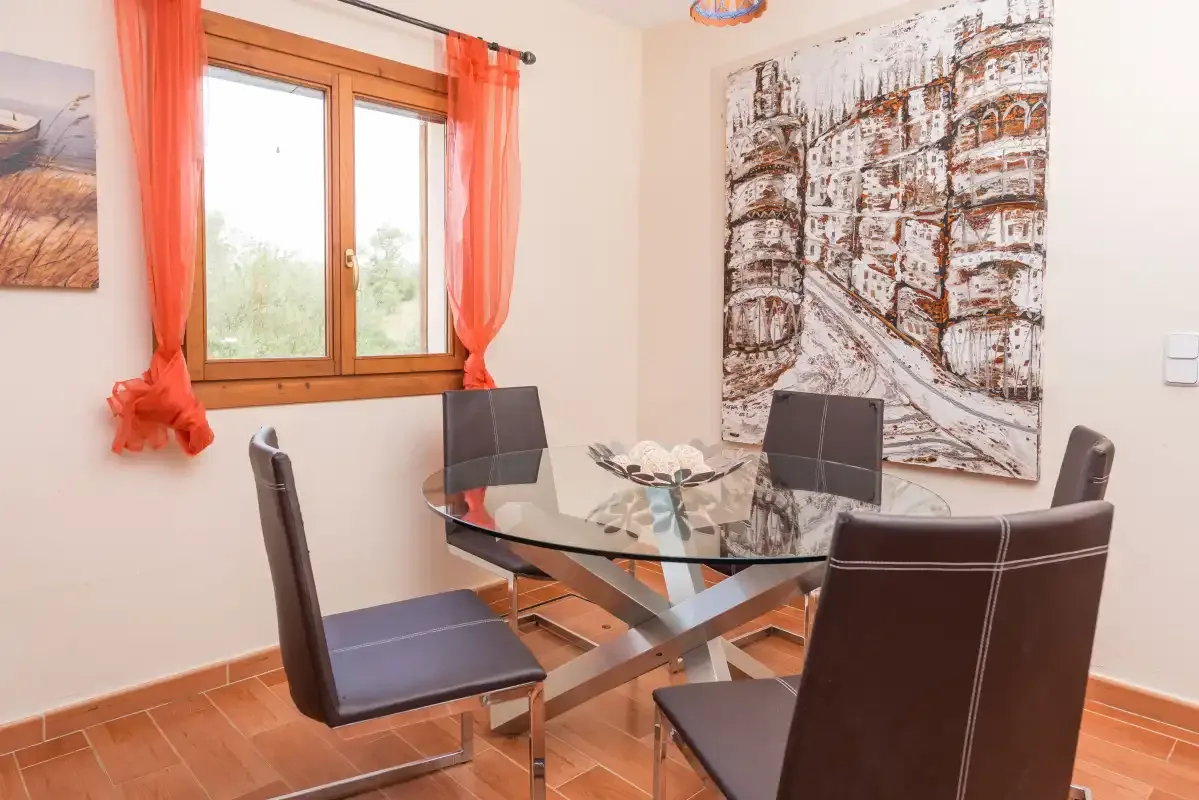 A dining area with a glass table and dark seating beside a window.