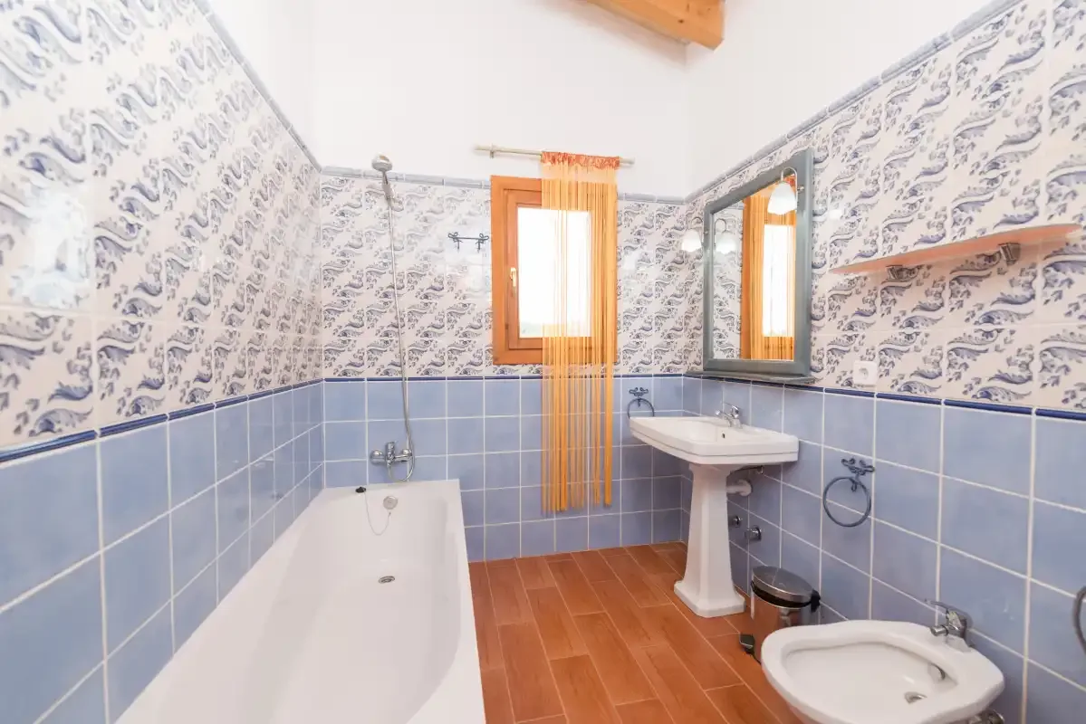A bathroom with a bathtub, pedestal sink, and patterned tile walls.