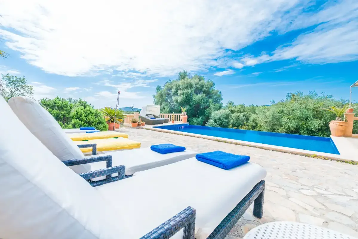A sunny poolside patio with cushioned loungers and a blue swimming pool.