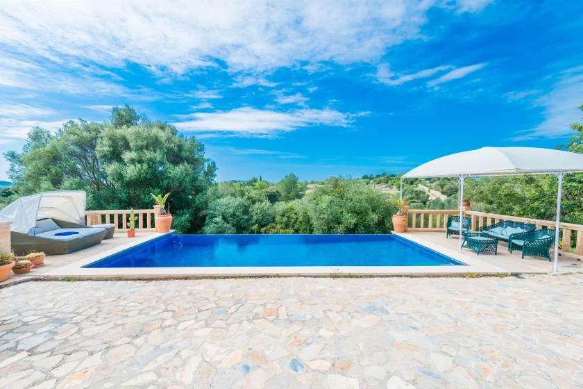 An outdoor swimming pool sits beside a covered patio with seating.