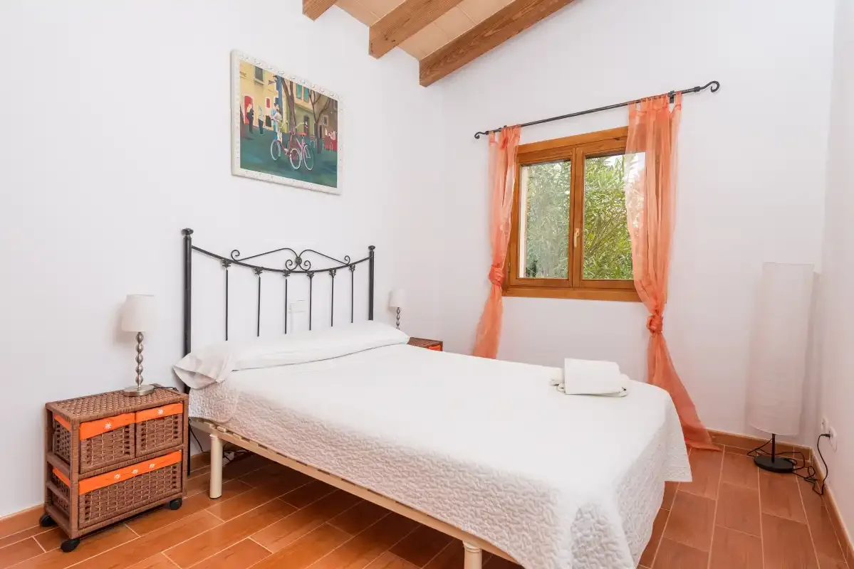 A bedroom with a double bed beneath a window with orange curtains.