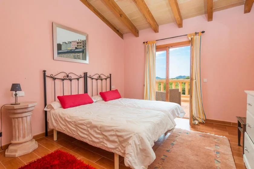 A bedroom with a bed, pink walls, and a glass door opening onto a balcony.