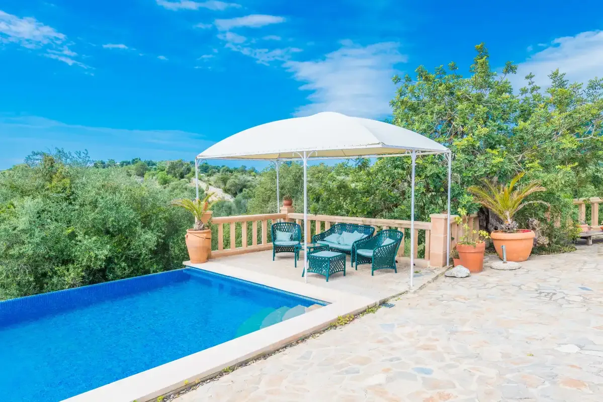 An outdoor swimming pool beside a shaded patio with seating and potted plants.