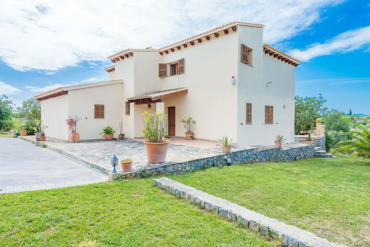 A white stucco house with terracotta roof tiles stands beside a green lawn.