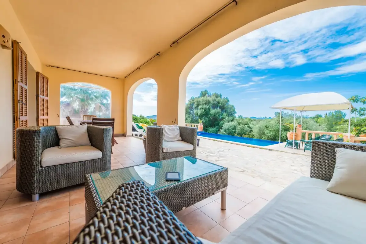A covered patio with seating overlooks a swimming pool and surrounding greenery.
