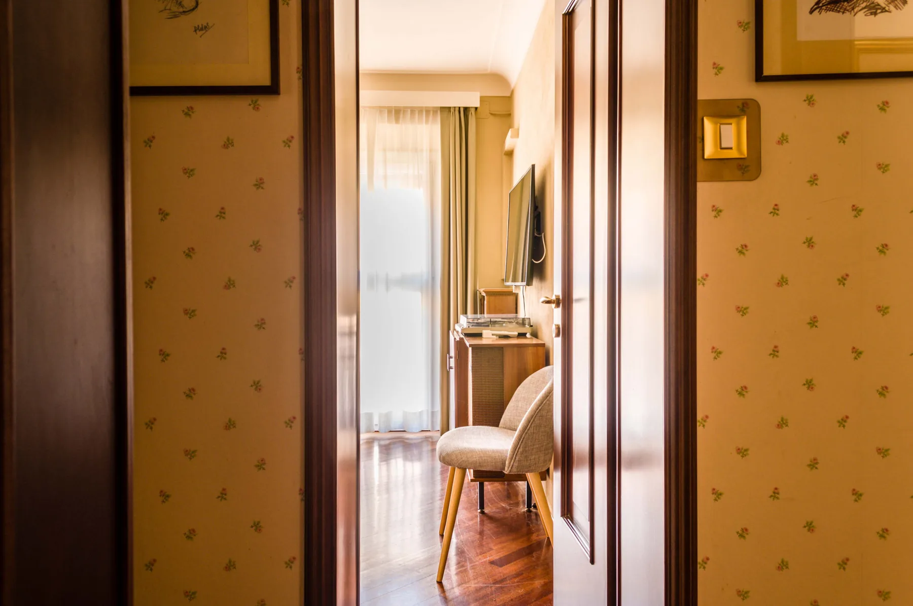 Una puerta da a una zona de estar con una silla y una ventana con cortinas.