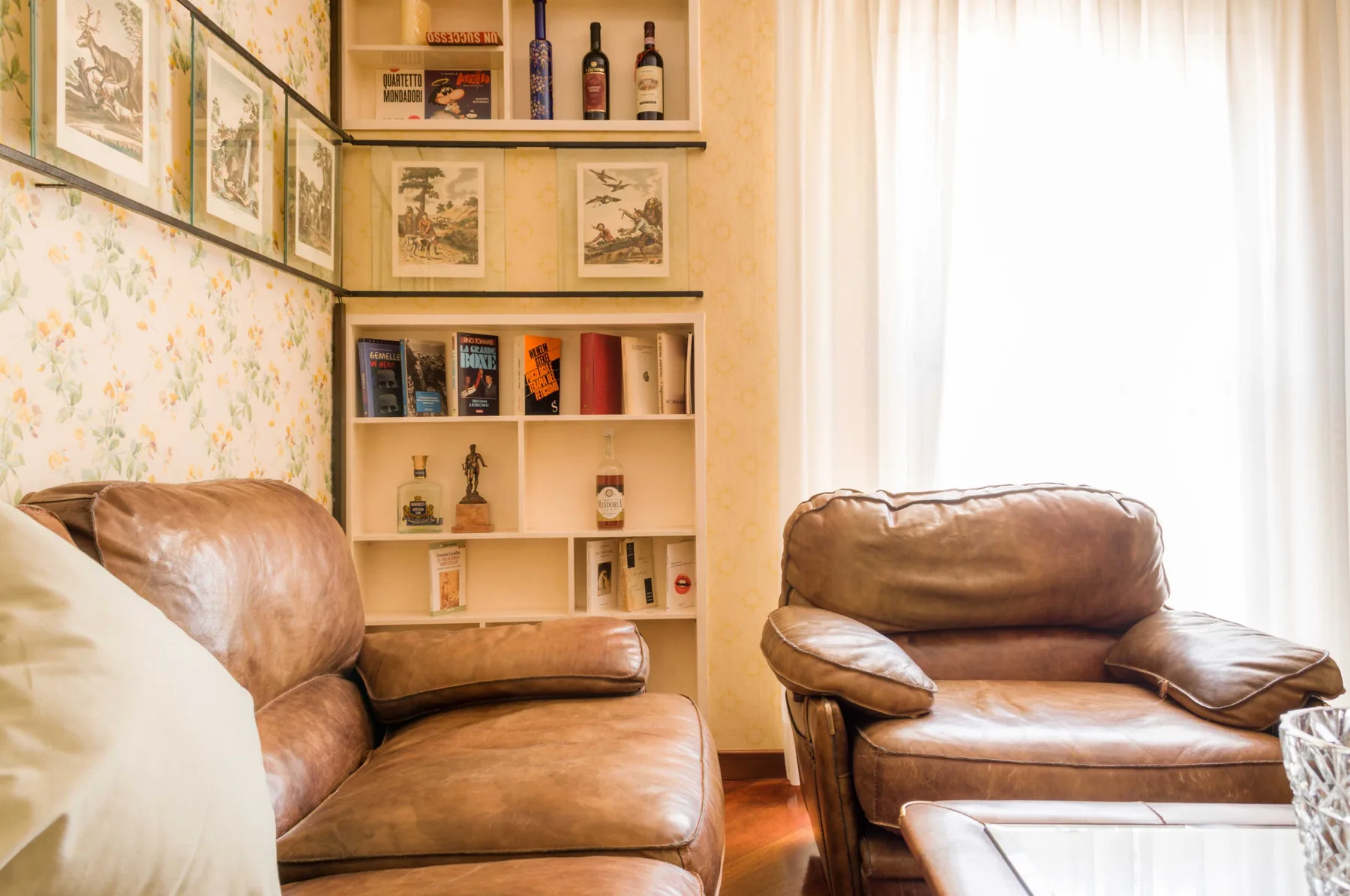 A sitting room with leather seating, built-in shelves, and a bright curtained window.