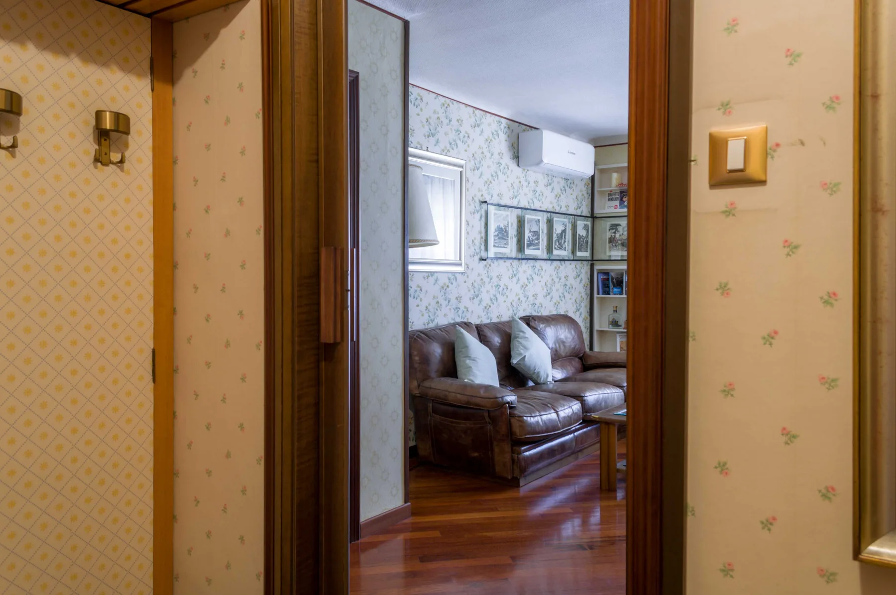 Una sala de estar con asientos, papel tapiz estampado y suelo de madera pulida.