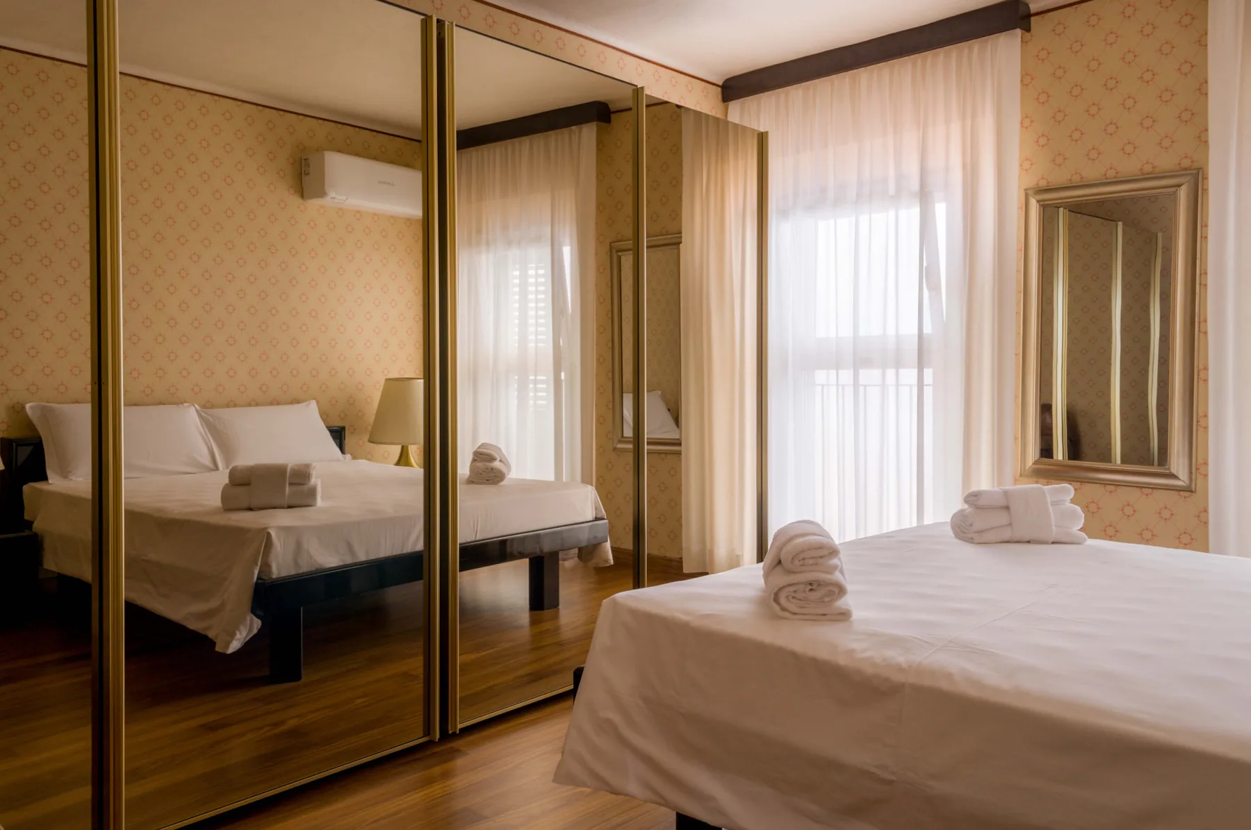 Un dormitorio con una cama grande, puertas de armario con espejo y una ventana luminosa.