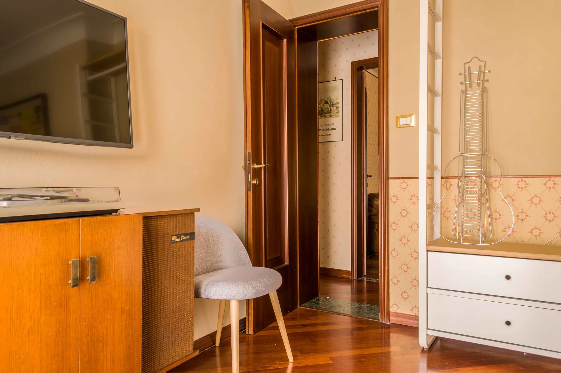 Una zona de estar en un dormitorio con un televisor sobre un mueble de madera y una puerta abierta.