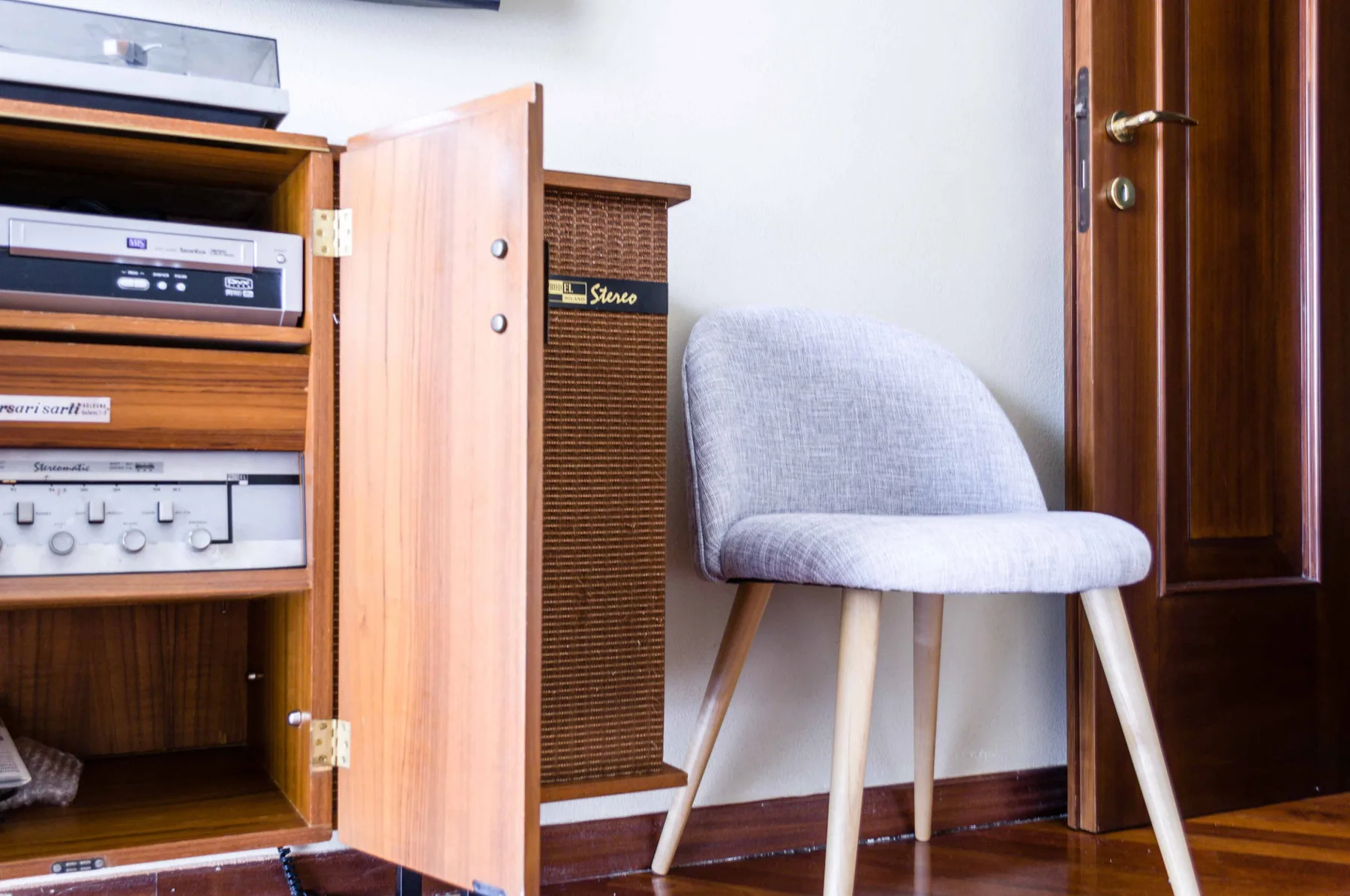 Una esquina de habitación con muebles de audio de madera y una silla tapizada gris.