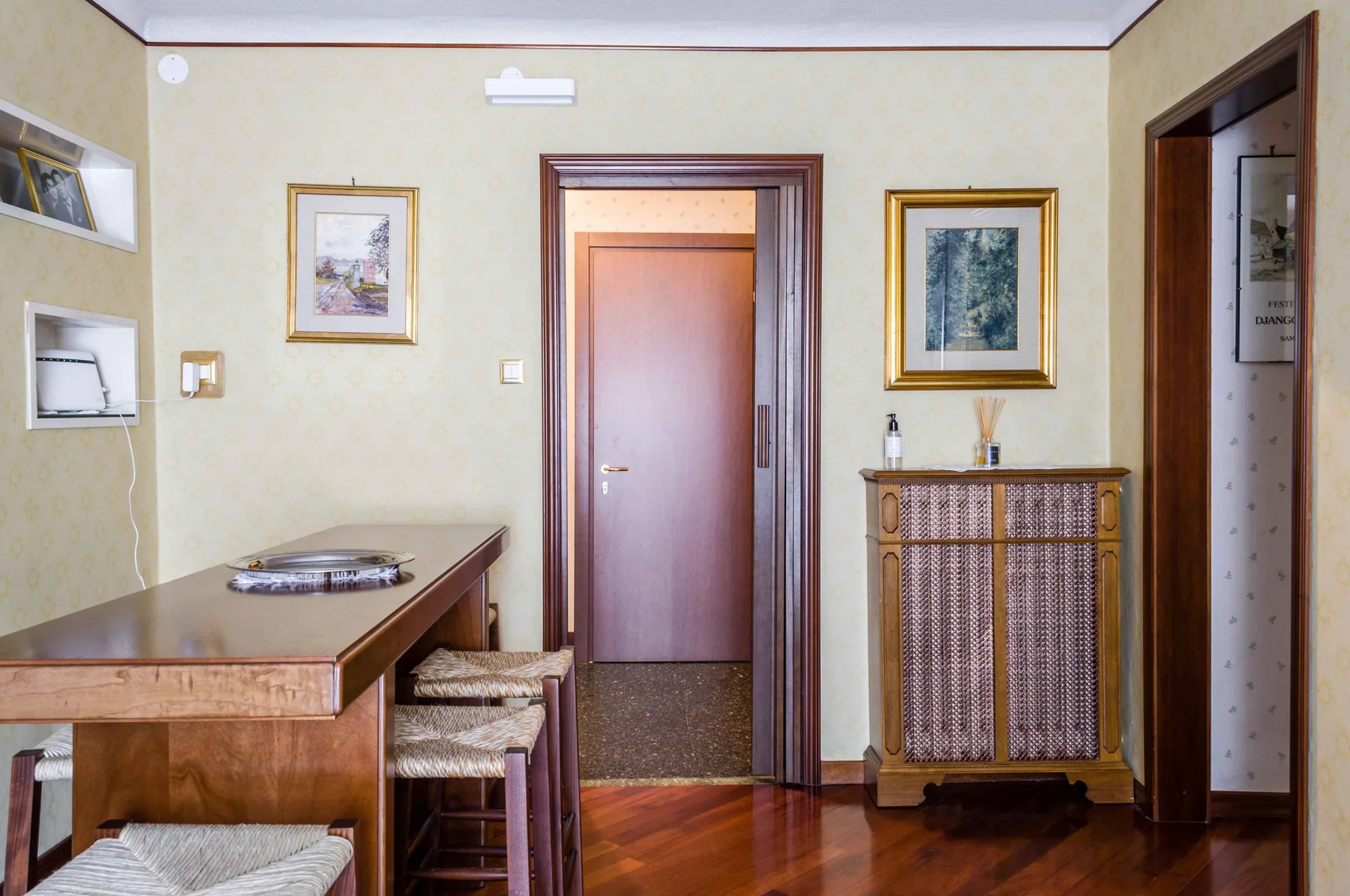Una habitación con un escritorio de madera, taburetes tejidos, cuadros y una puerta cerrada.