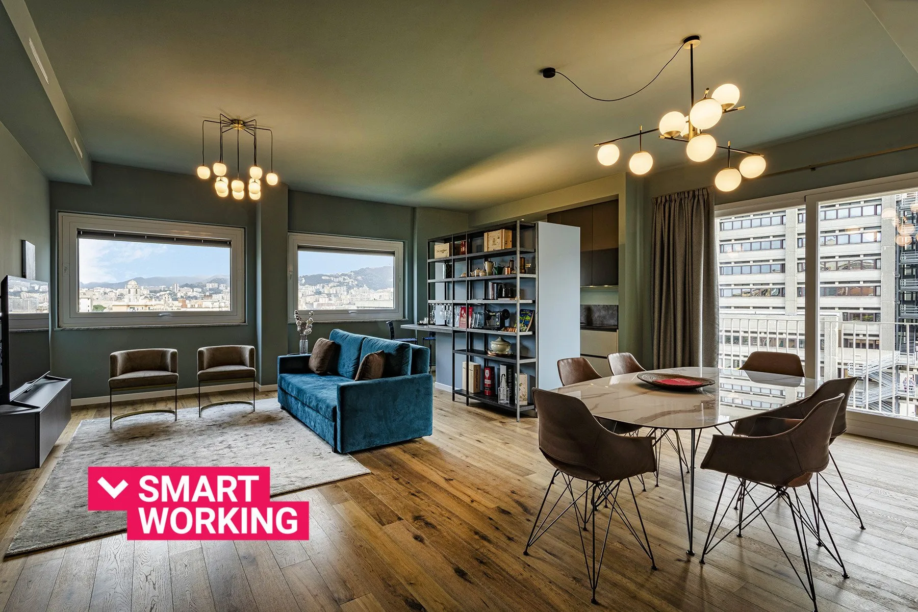 A living room with seating, bookshelves, and a dining table beside large windows.