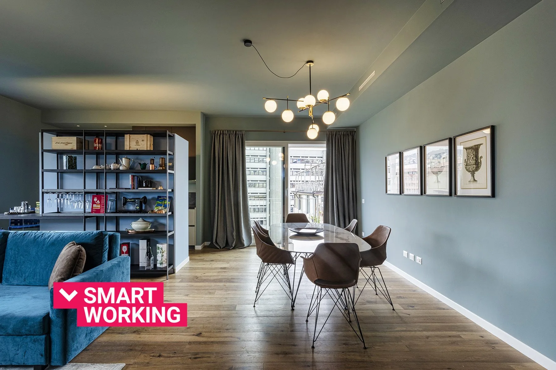 A dining area with a table and chairs sits beside a blue sofa and shelving.