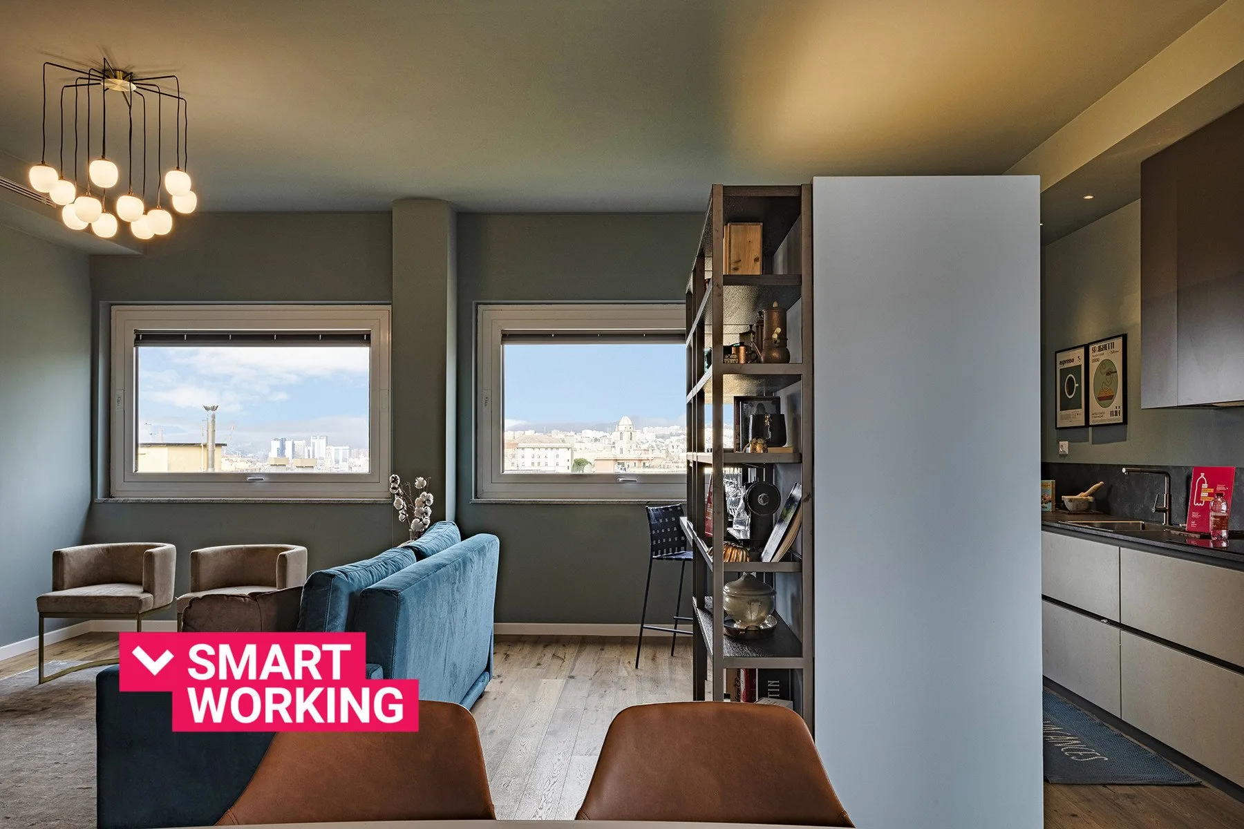 A living area with blue seating and two large windows overlooking the city.