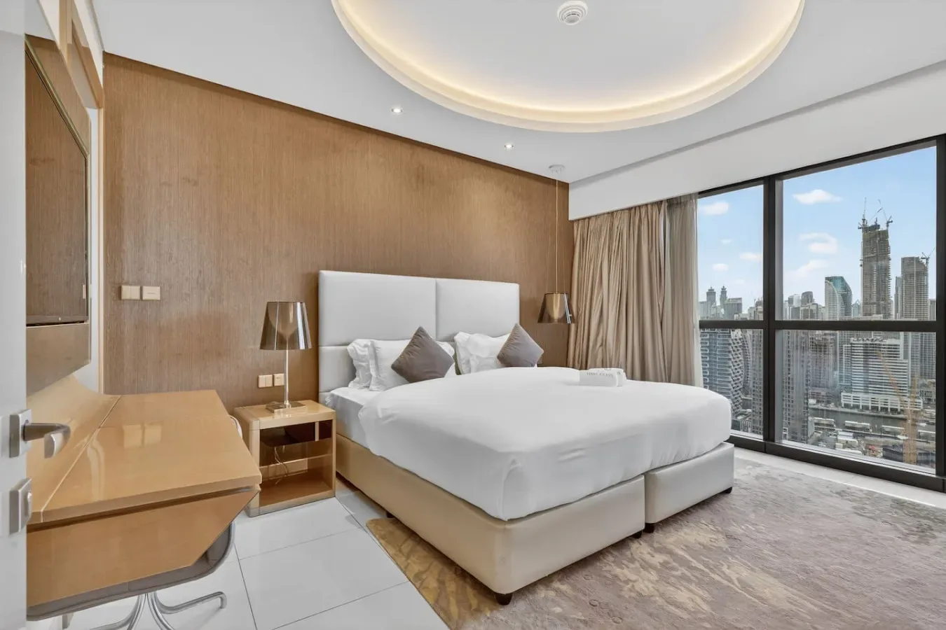 A bedroom with a large bed beside floor-to-ceiling windows overlooking the city.