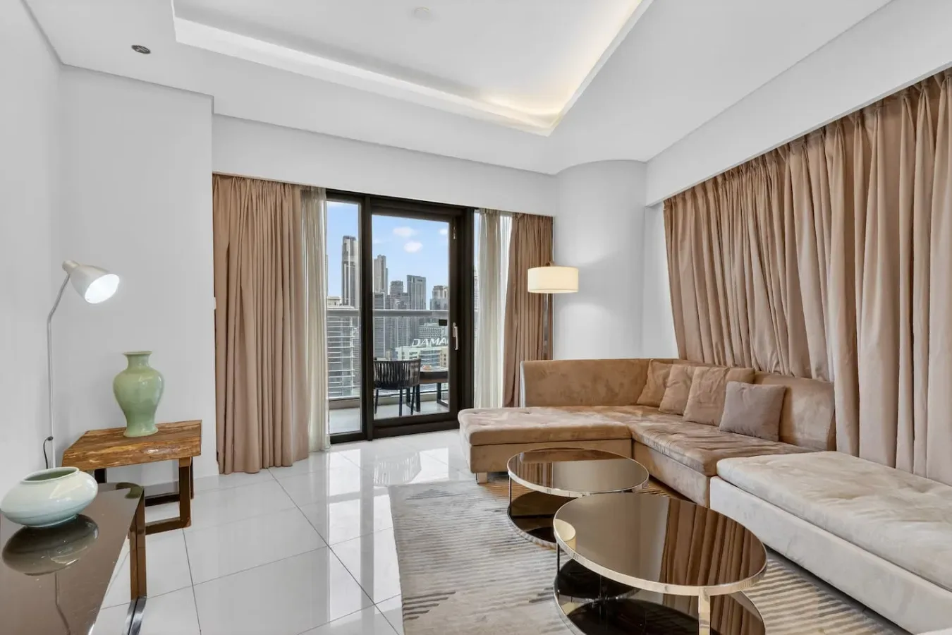 A bright living room with a sectional seating area and large curtained windows.
