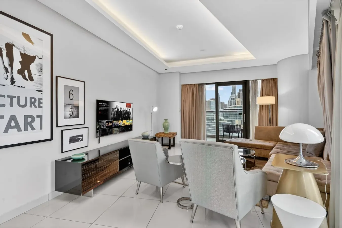 A modern living room with seating, a television, and large windows overlooking the city.